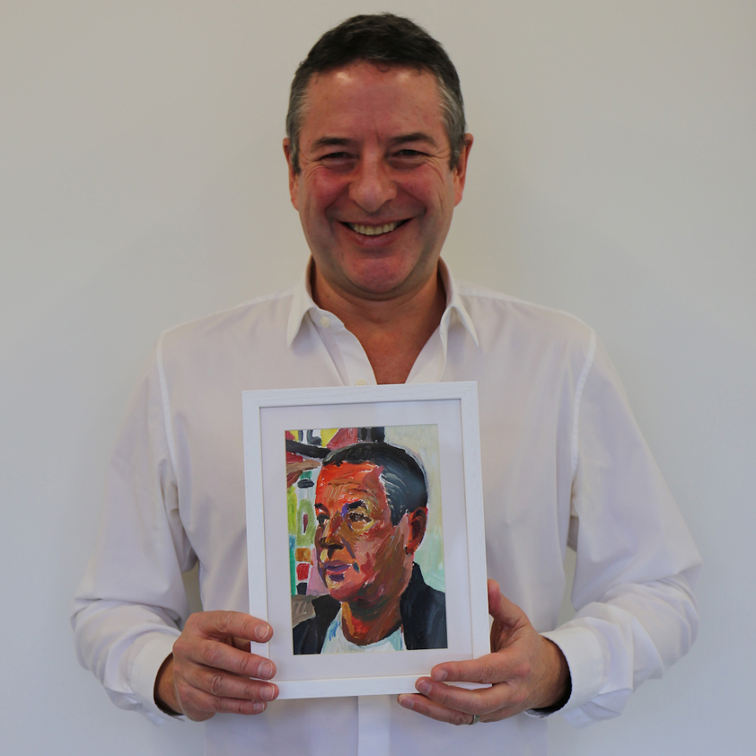 Photo of a man sitting in an office holding his painted portrait